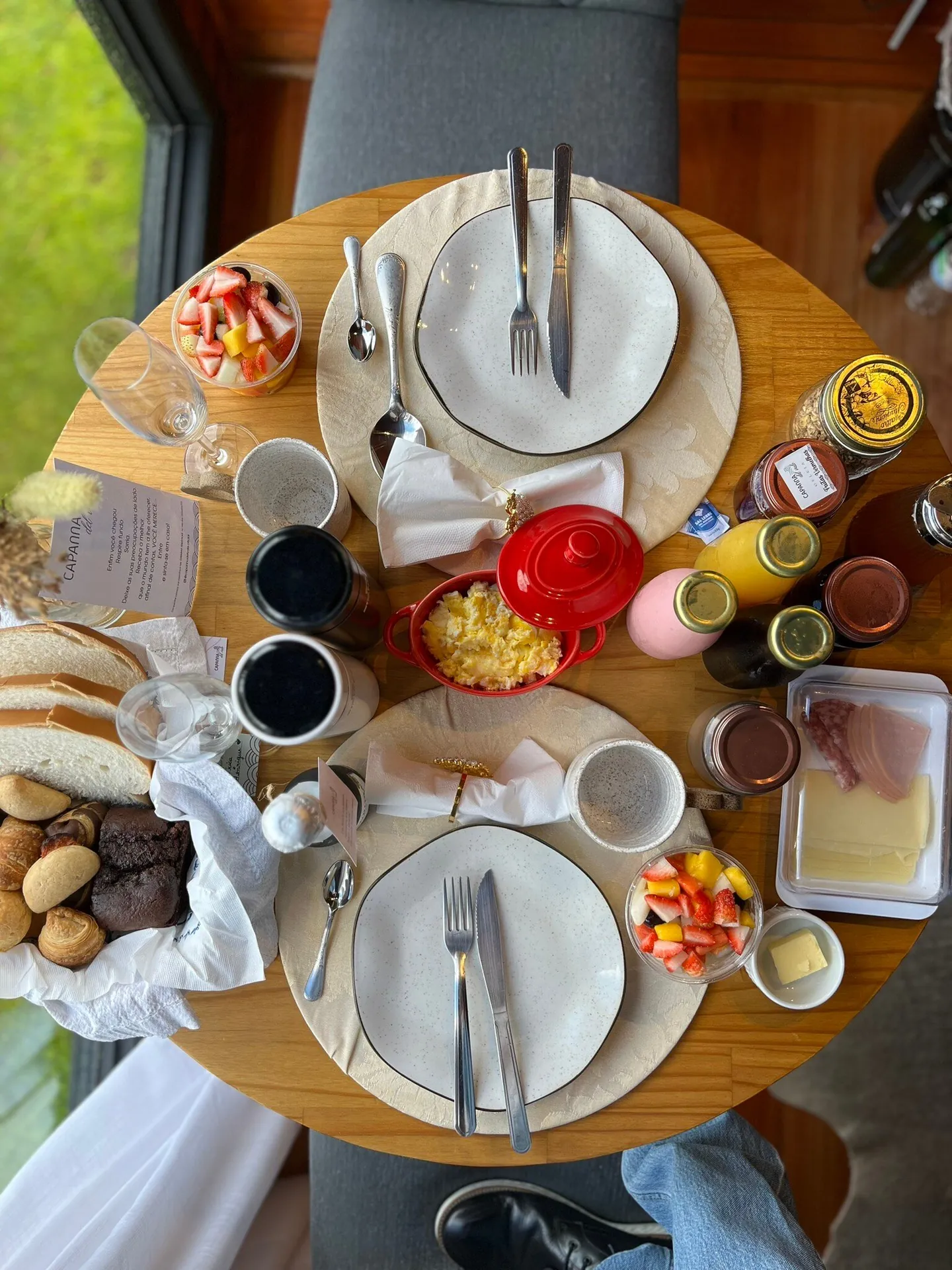 Mesa do café da manhã vista de cima, com pães, frutas e geleias